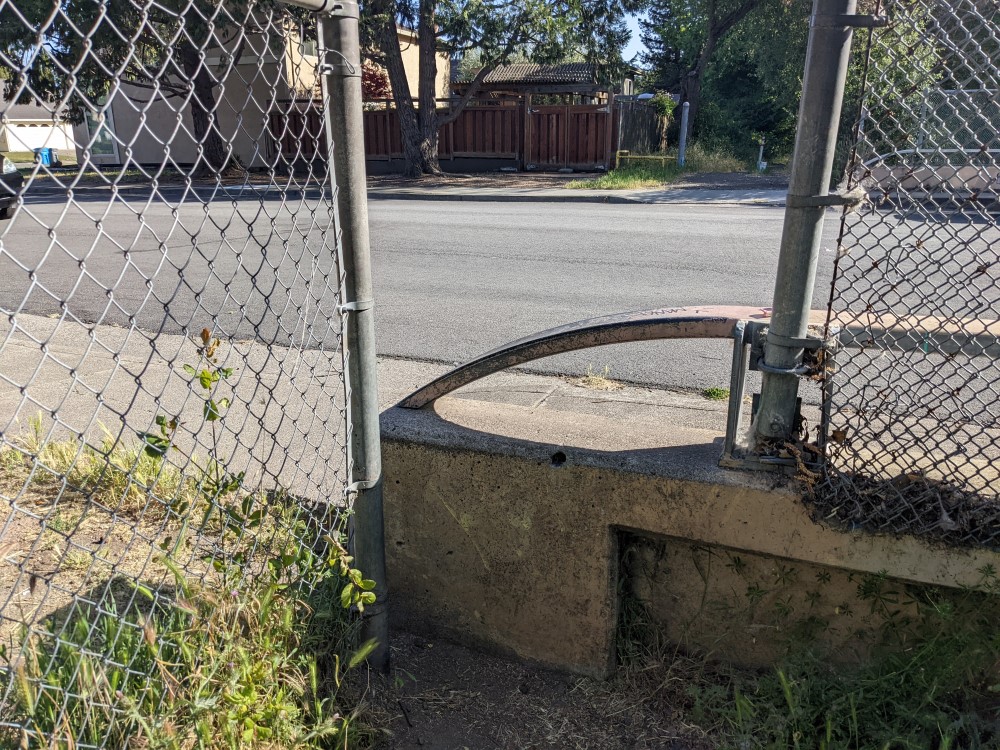 A fence, with a gap in it, but the gap has a metal railing about waist height. On the other side is a road